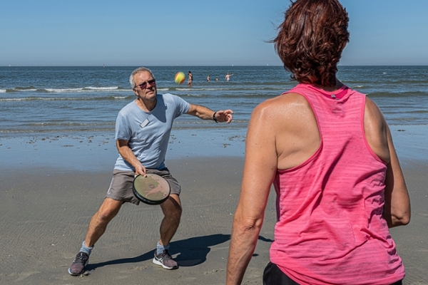 Eine Gruppe von Patientinnen und Patienten stehen in einem Kreis und machen Sport am Strand