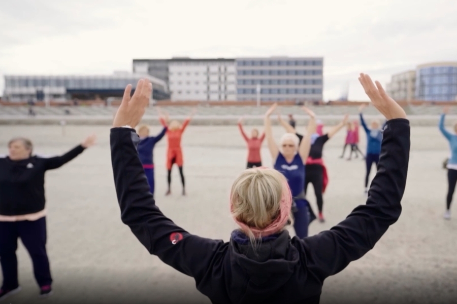 eine Gruppe macht Sport am Strand. Die Klinik Norderney sieht man im Hintergrund 